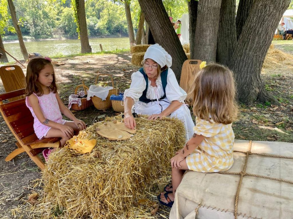 A River Runs Thru History reenactor, Lynn Persico (center) shows children how to play a game with rocks last year. (File photo)