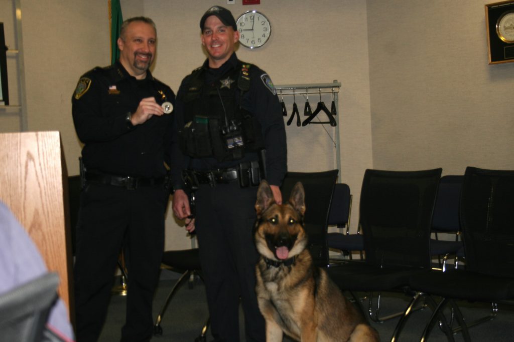 Police Chief Dan Vittorio holds up the badge as officer Robert Carroll has Thor, the department's new canine officer, on a leash during the Oak Lawn Village Board meeting on November 22. (Photo by Joe Boyle)