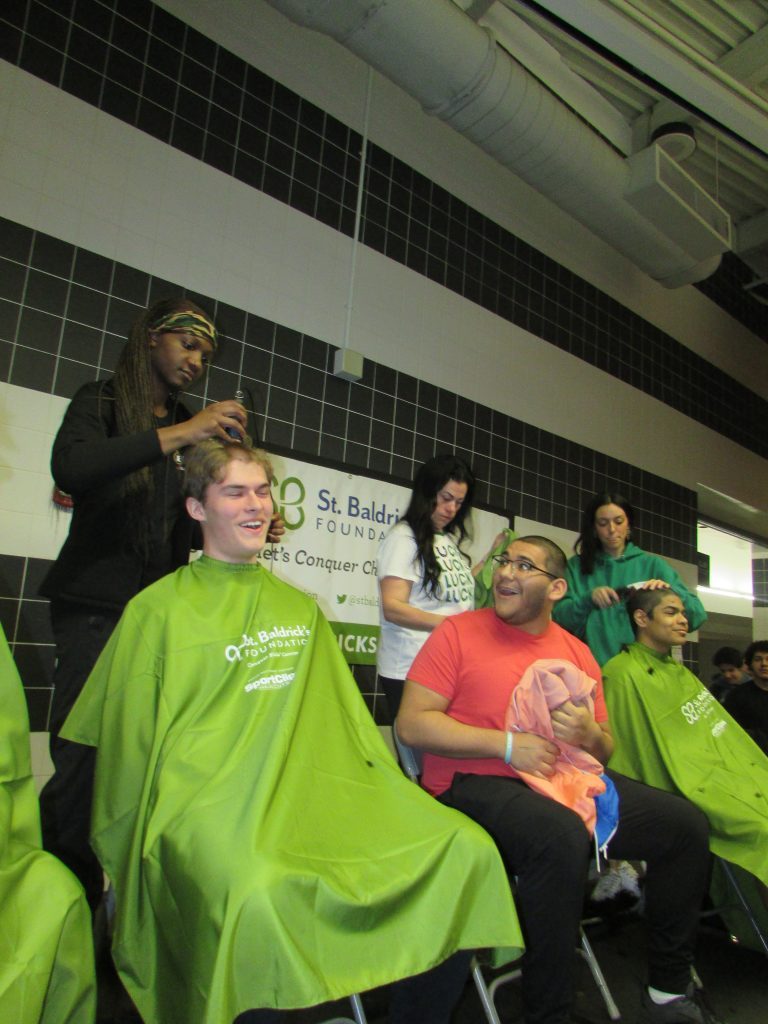 Freshly shaved Stagg High School junior Oswaldo Macias, of Bridgeview, reacts as he watches his classmate Max Slanda, of Orland Park, gets his St. Baldrick's haircut at the Palos Hills school on St. Patrick's Day. (Photos by Dermot Connolly)