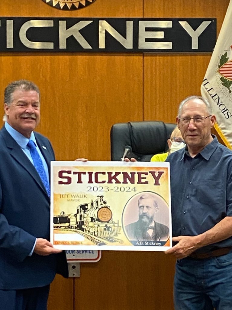 Mayor Jeff Walik (left) presents Bob Behounek a large replica of the village sticker Behounek designed. (Supplied photos)