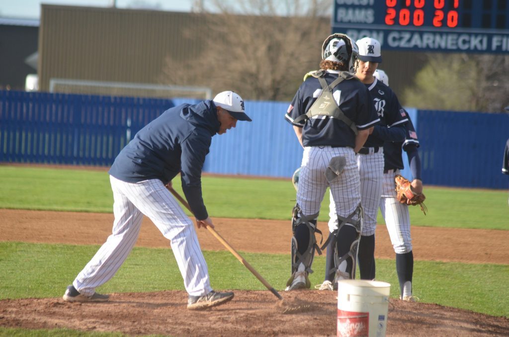 Reavis baseball coach Don Erickson rakes a soggy mound during a game against Evergreen Park on April 12. The longtime Rams coach is retiring after this season. Photo by Jeff Vorva