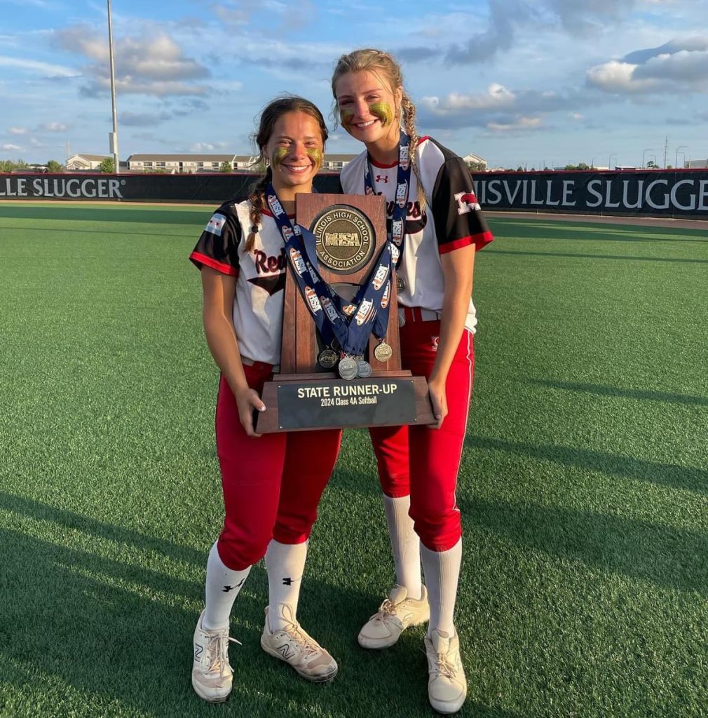Marist seniors Caroline O’Brien (left) and Camryn Lyons hold the Class 4A state runner-up trophy after St. Charles North defeated the RedHawks, 7-2, in the championship game on June 8 in Peoria. Photo courtesy of Marist High School Athletics